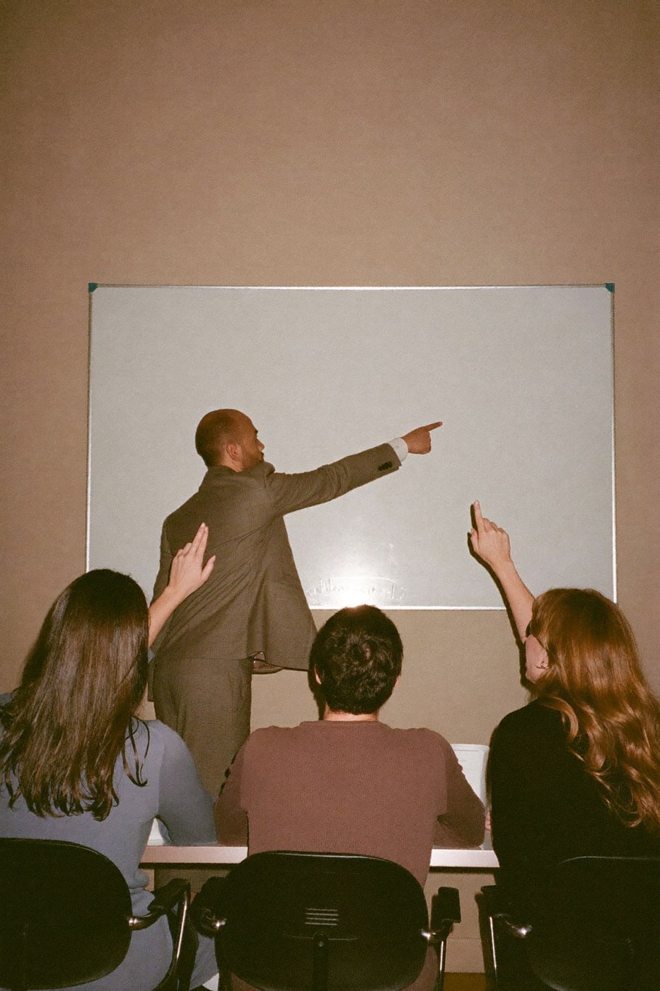 Presenter pointing at an empty whiteboard while colleagues nod