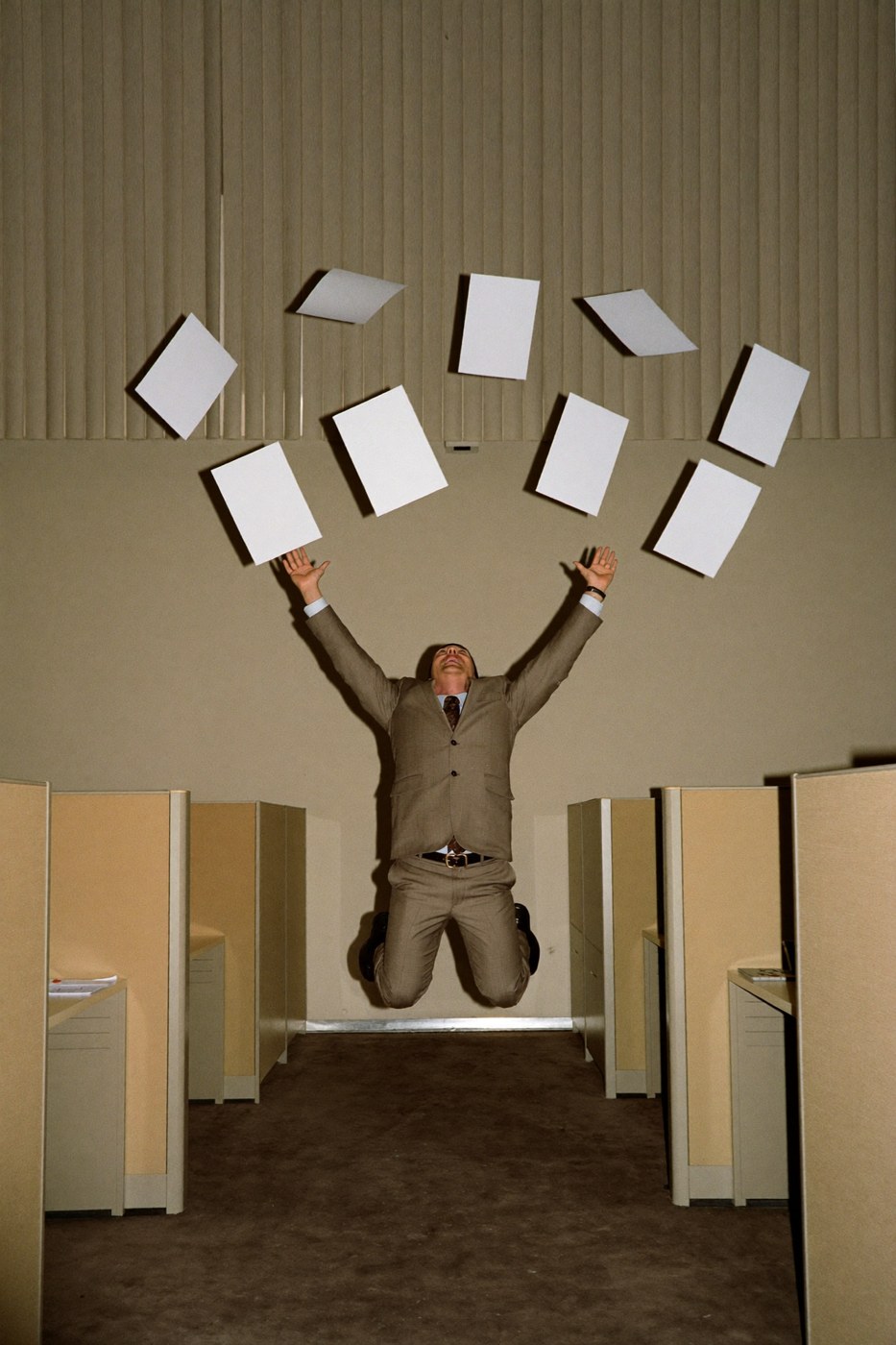Office worker jumping in a cubicle aisle throwing blank papers