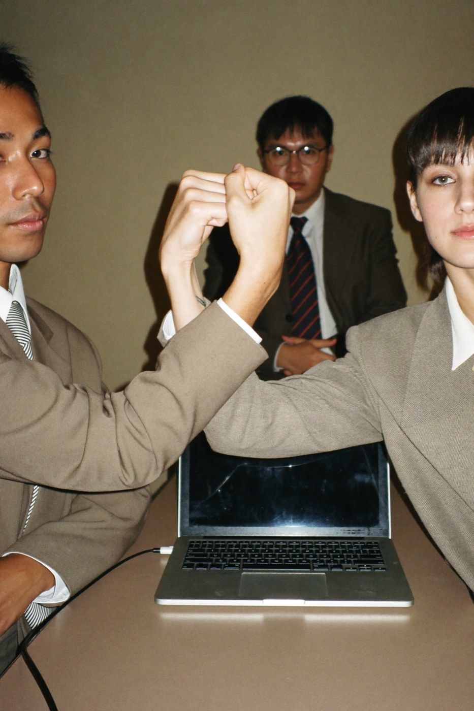 Two coworkers fist bumping gravely over a laptop while a third watches